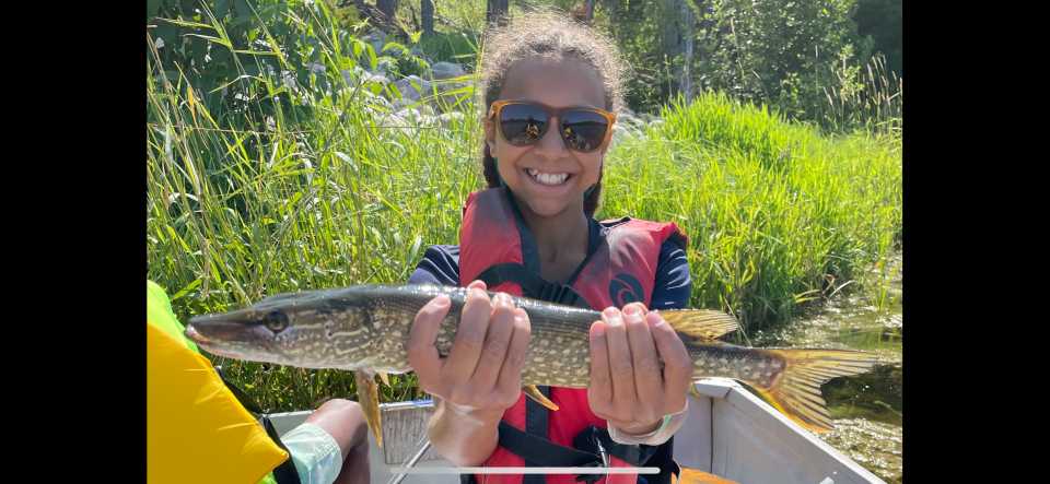 A girl smiles brightly while holding her fishing catch